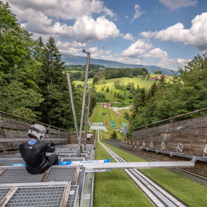 Skisprungschanze, Skispringer sitzt auf Anlaufbakken.